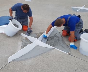 Zwei Mitarbeiter bei der Sanierung eines Betonbodens mit Spachtel