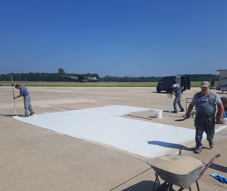 Mehrere Mitarbeiter bei der Sanierung eines Flugplatzes vor blauem Himmel im Hintergrund